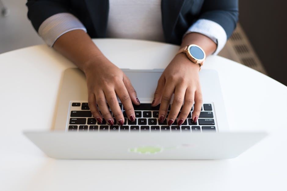 Hands typing on laptop keyboard, person wearing smartwatch and dark blazer